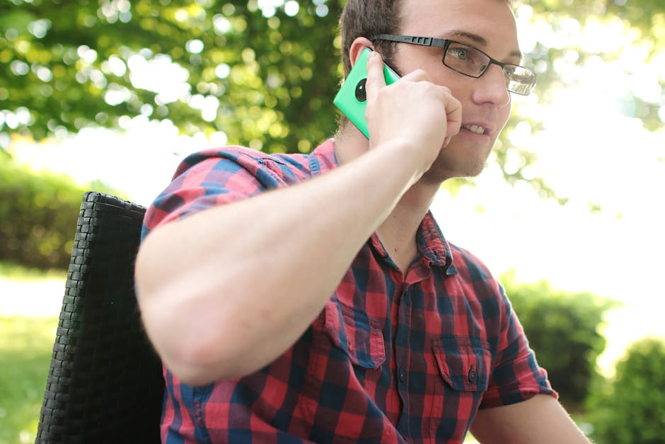 Casual man in plaid shirt having a phone conversation in a sunny park setting.